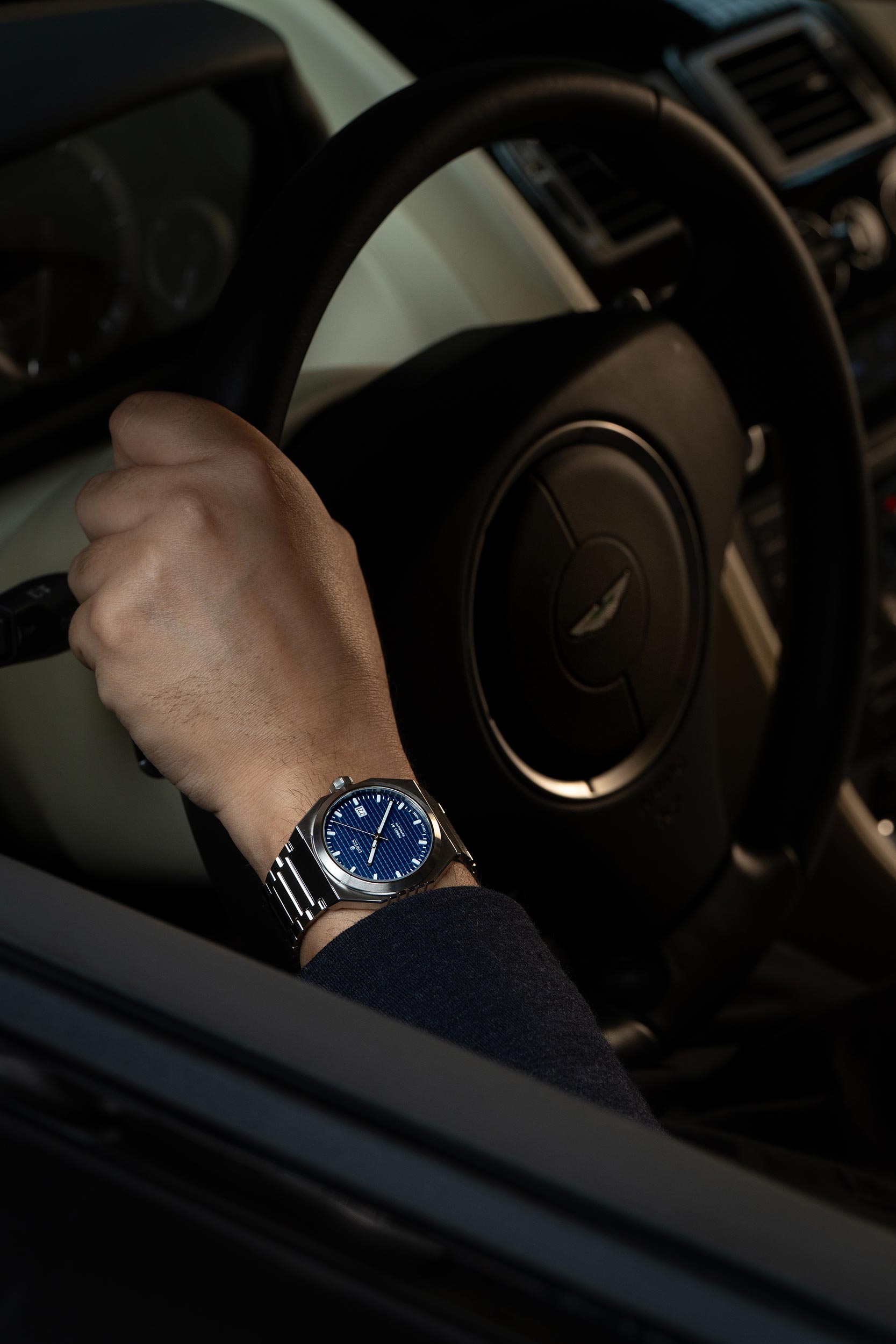Hand wearing a watch on a Austin Martin dashboard Model DWISS A1- using a Swiss made automatic movement La Joux-Perret G100 Soigné with 68 hours power reserve and white superLumiNova blocks