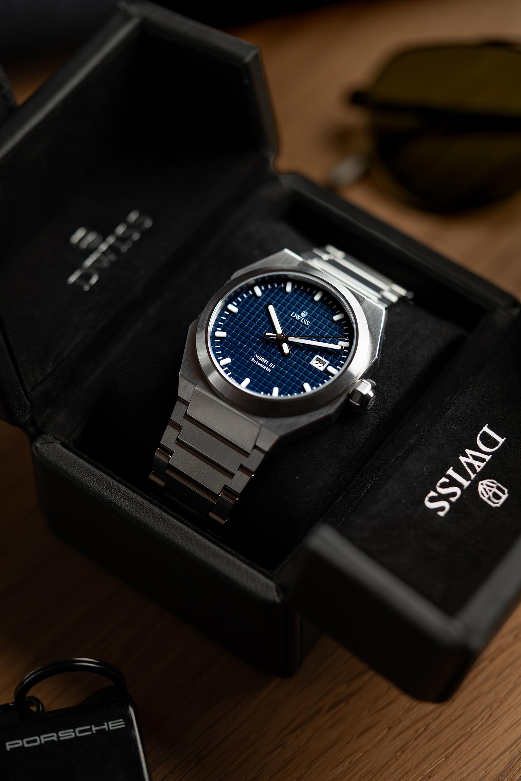 Luxury watch with blue dial in a branded box on a wooden surface. Model DWISS A1- using a Swiss made automatic movement La Joux-Perret G100 Soigné with 68 hours power reserve and white superLumiNova blocks