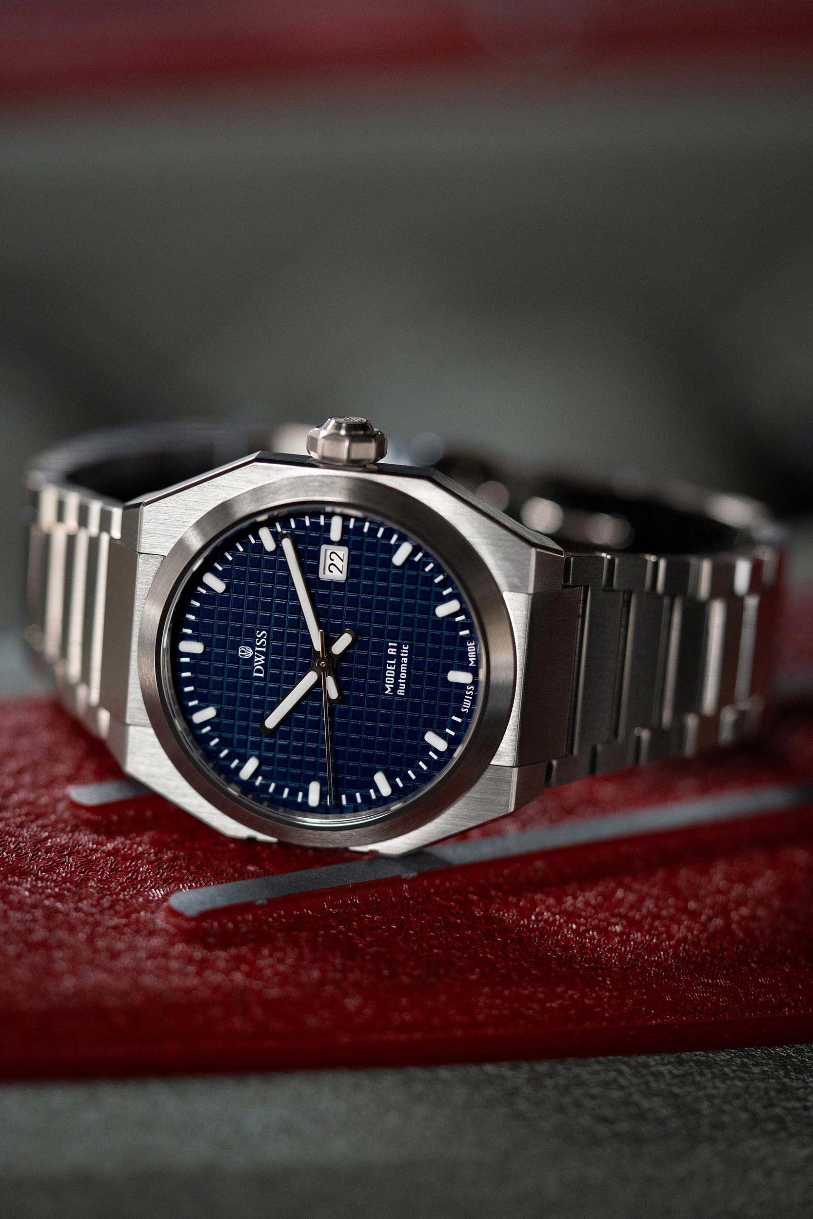 Silver watch with blue dial on a red Ferrari engine. Watch model DWISS A1- using a Swiss made automatic movement La Joux-Perret G100 Soigné with 68 hours power reserve and white superLumiNova blocks