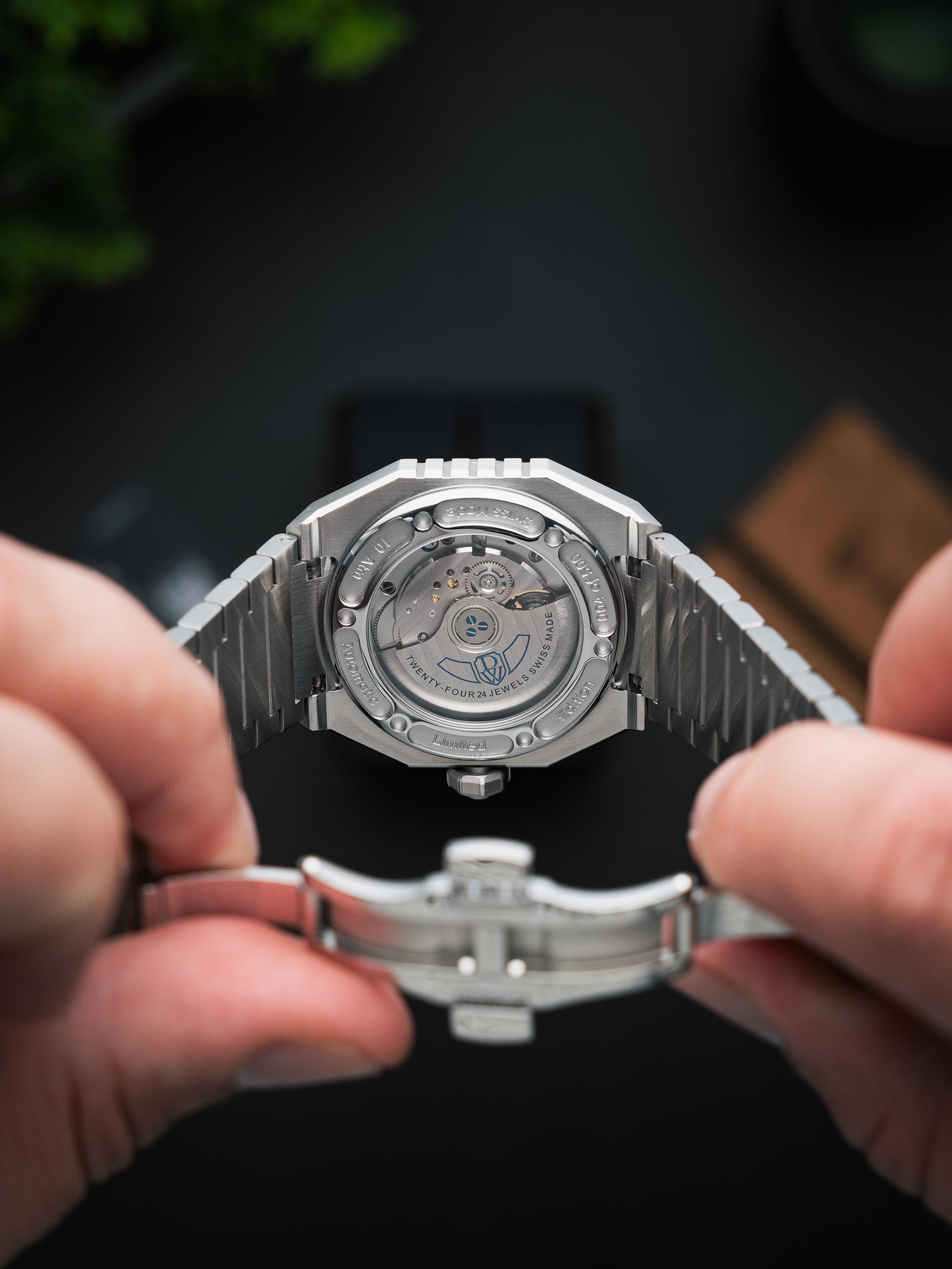 Silver watch with a visible brand logo DWISS held by two hands against a dark background. Model DWISS A1- using a Swiss made automatic movement La Joux-Perret G100 Soigné with 68 hours power reserve and white superLumiNova blocks
