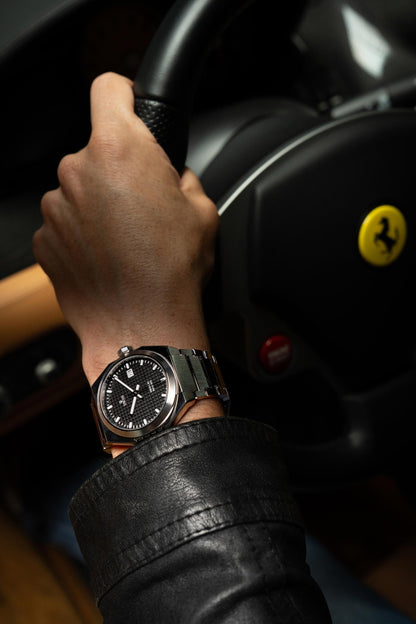 Hand wearing a watch on a Ferrari steering wheel with a Ferrari logo. Model DWISS A1- using a Swiss made automatic movement La Joux-Perret G100 Soigné with 68 hours power reserve and white superLumiNova blocks