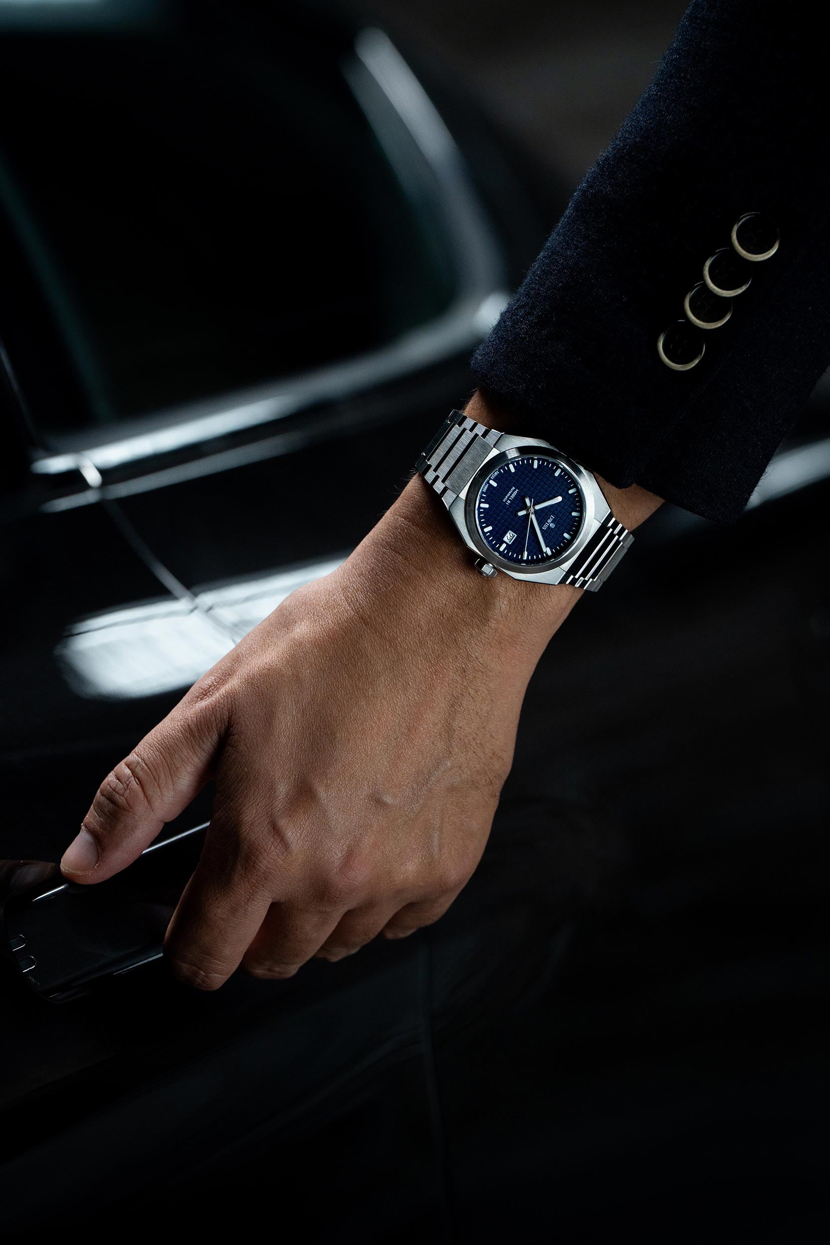 Hand wearing a silver watch on a car door handle with a dark background. Model DWISS A1- using a Swiss made automatic movement La Joux-Perret G100 Soigné with 68 hours power reserve and white superLumiNova blocks