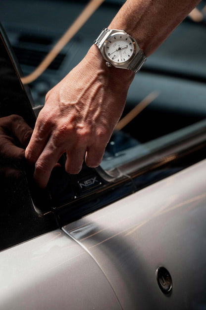 Hand with a silver watch on a car window, possibly opening a door. Model DWISS A1- using a Swiss made automatic movement La Joux-Perret G100 Soigné with 68 hours power reserve and white superLumiNova blocks