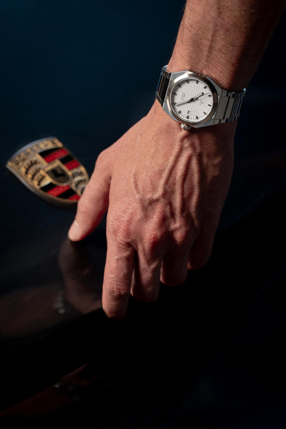 Hand wearing a silver watch with a dark background opening a Porsche Model DWISS A1- using a Swiss made automatic movement La Joux-Perret G100 Soigné with 68 hours power reserve and white superLumiNova blocks