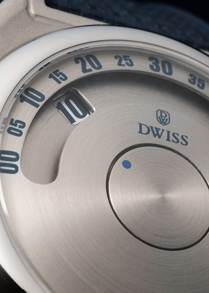 DWISS S1 Wandering Horas dial circular cepillado. Cierre de un dial de plata cepillado con números azules, una ventana de fecha, y el logotipo DWISS impreso en la cara.